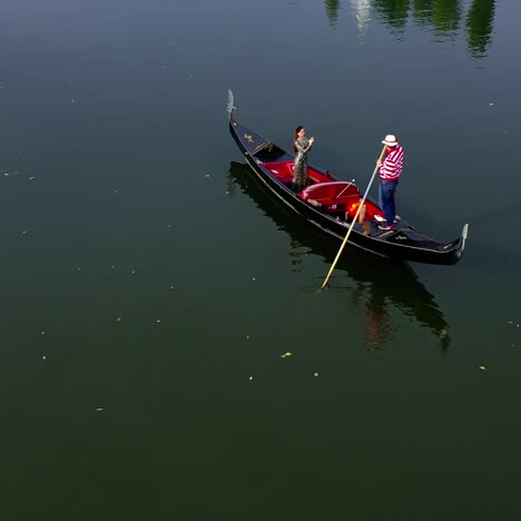gondolier riding a boat with a woman. beautiful lady travelling in gondola along the river at sunset. aerial view. camera motion around.