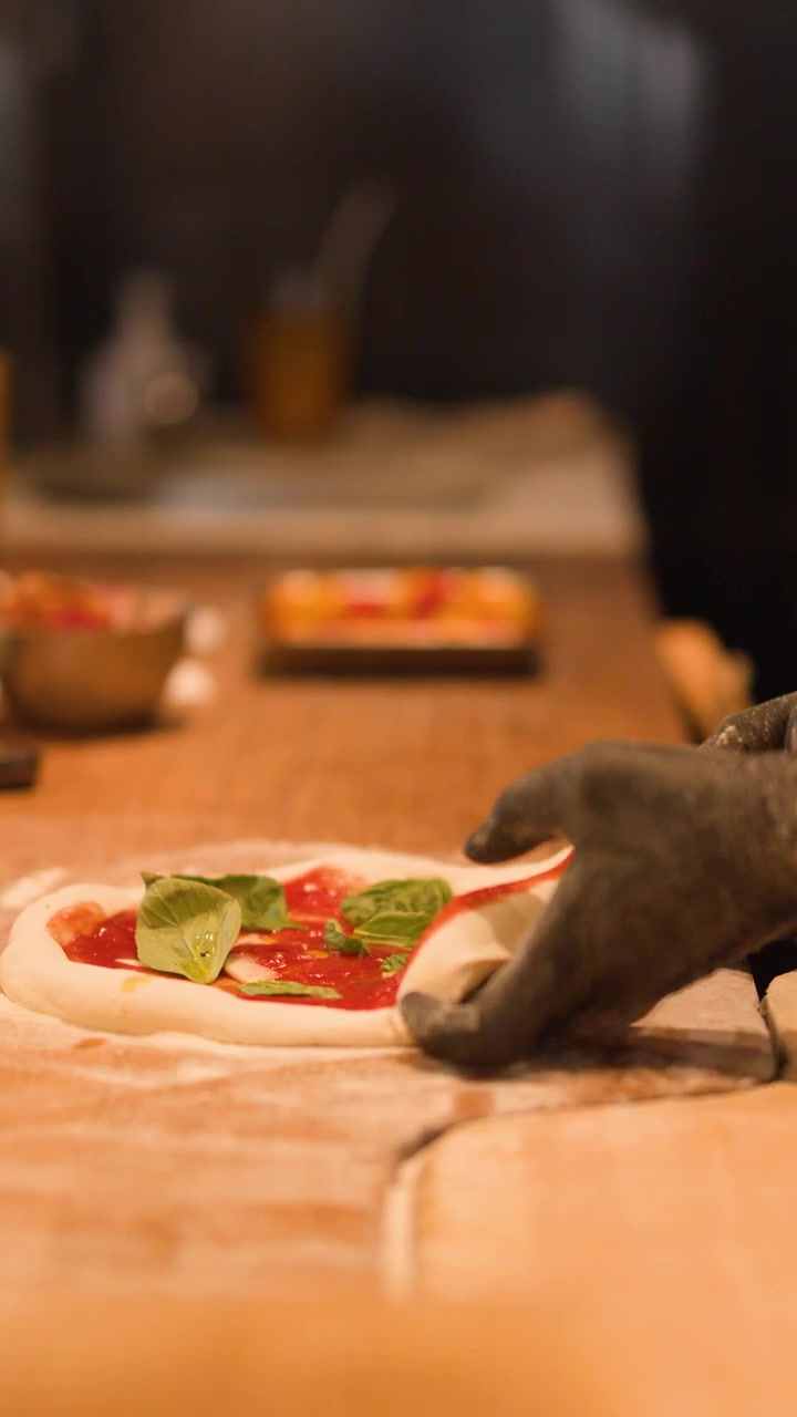 Primo piano di mani guantate che preparano impasto fresco per pizza su un bancone da cucina di ristorante infarinato