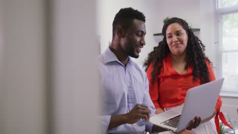 Two-happy-diverse-business-people-working-together,-using-laptop-in-modern-office