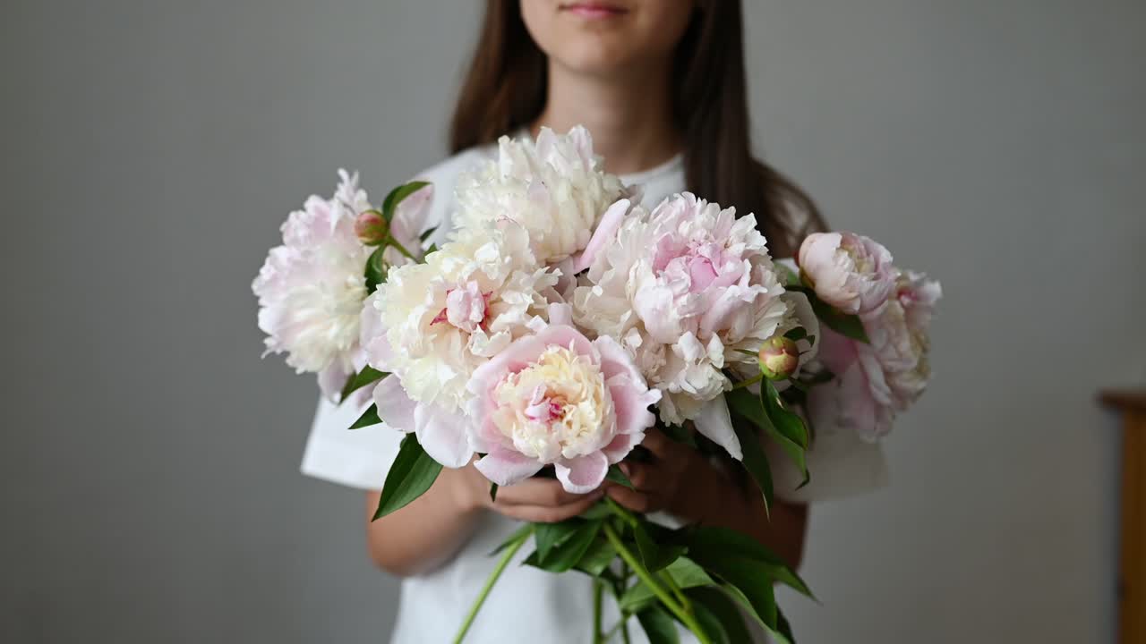 Bambina in piedi con un fiore di peonia in fiore con stelo