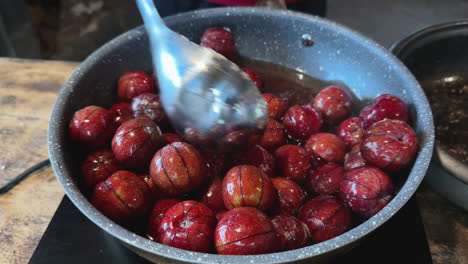 cooking process of ripe red plums in boiling syrup using a ladle in a rustic kitchen