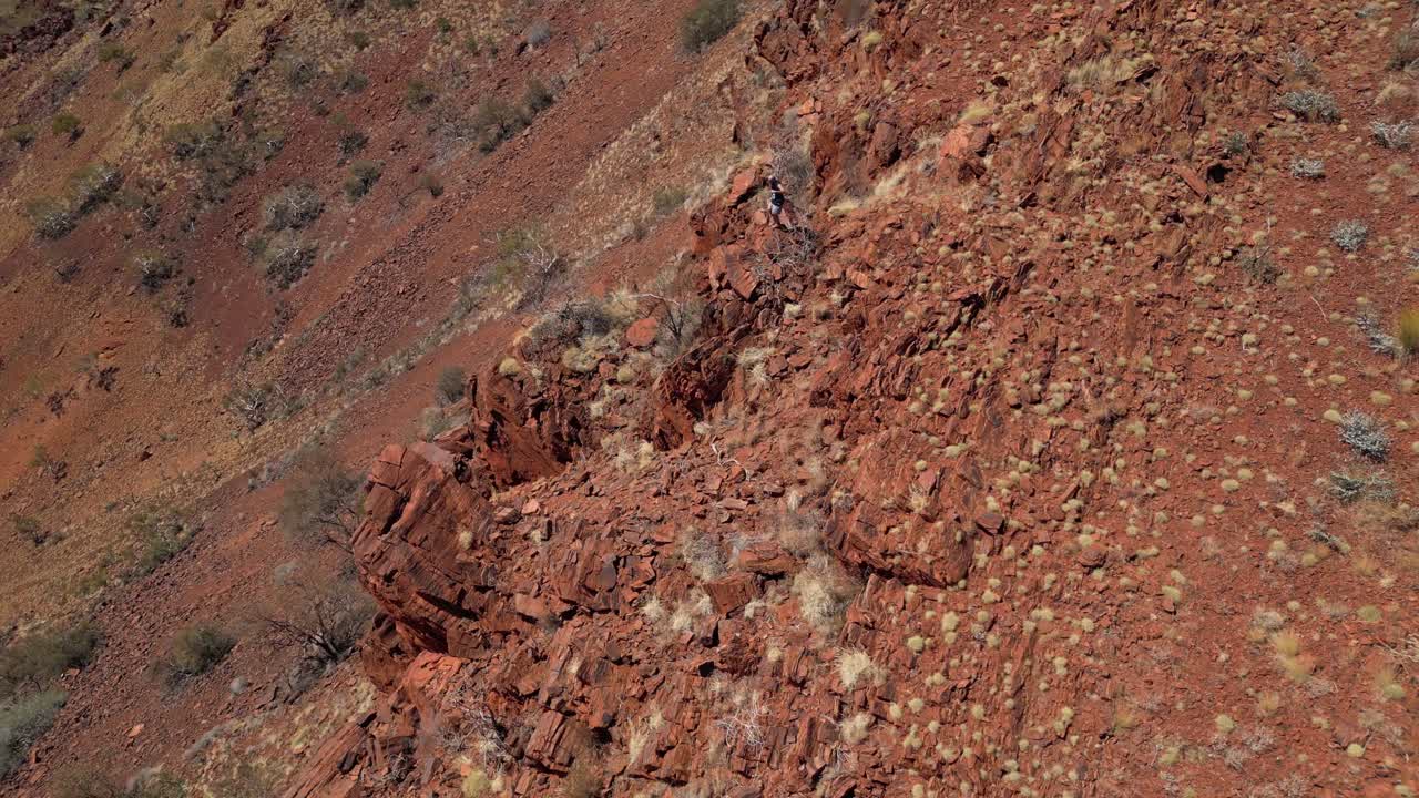 hombre caminando por el borde de la montaña rocosa durante una aventura de senderismo en el desierto de australia occidental
