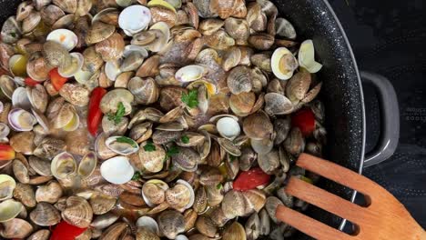 stirring delicious fresh shell clams and tomatoes with wooden forks in hot pan