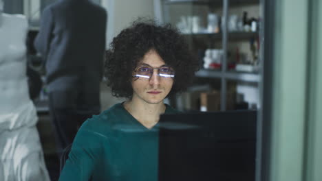man with curly hair and glasses working on a computer in a lab
