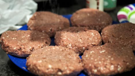 seasoning plant based burger patties on a blue plate for a summertime barbecue cookout, close up shot in 60 frames per second 4k