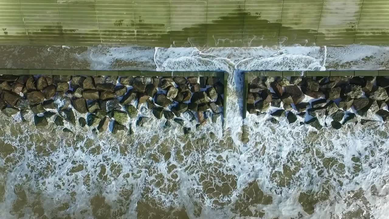 Topshot of waves hitting the sea defences. The waves are surging over the barrier and crashing into the concrete wall