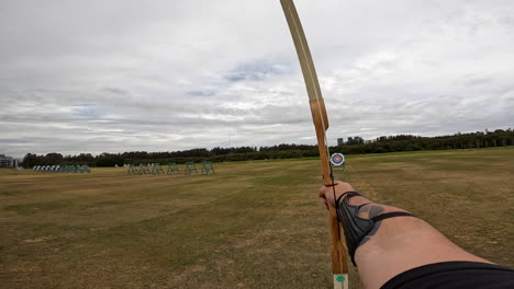 pov un arquero dispara flechas desde su arco a un objetivo en el campo de tiro con arco