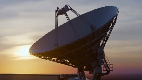 large satellite dish silhouetted against a sunset or sunrise sky