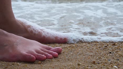 low angle shot of a barefoot woman cooling her feet into the low tide waves seawater in hong kong