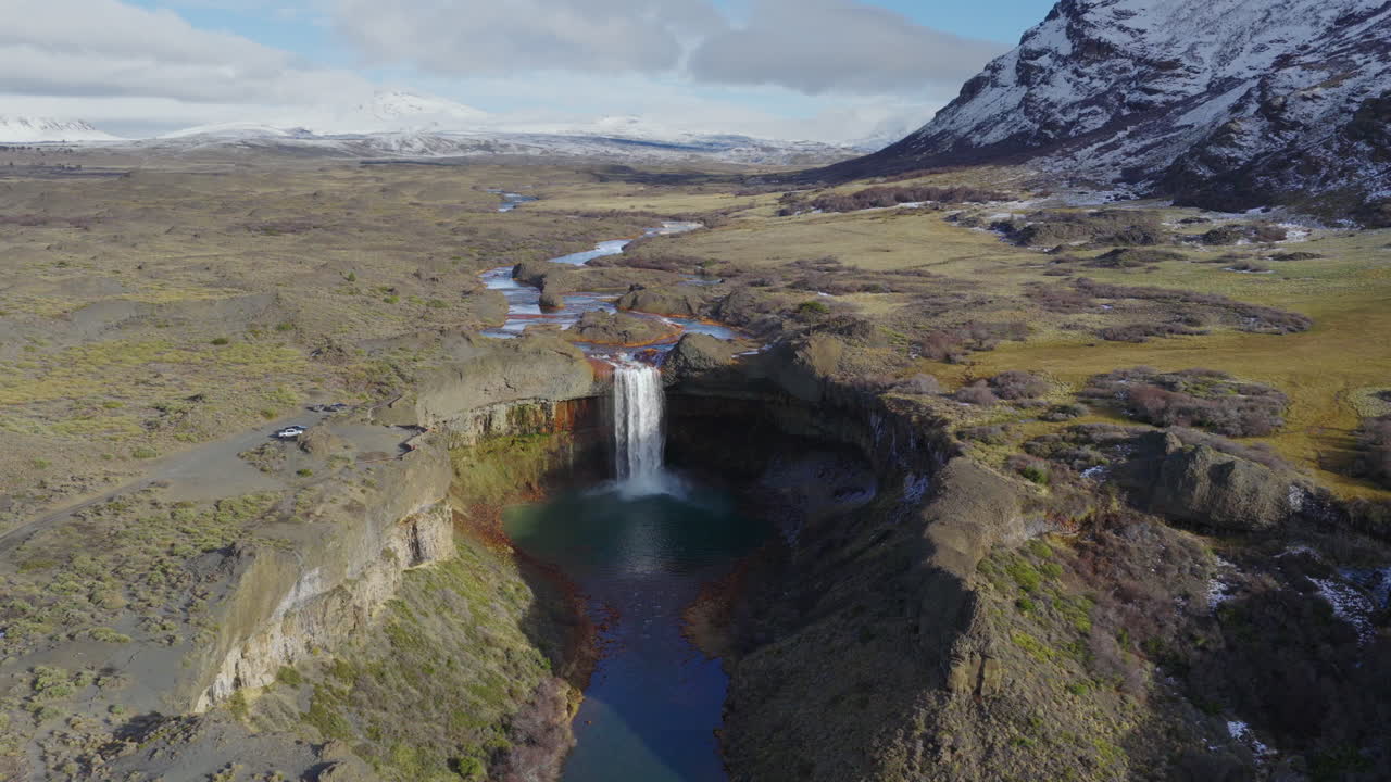 Drone orbit captures Agrio Waterfall plunging into a basalt pool near Caviahue, Neuquén, Argentina, with barren slopes of Cerro Caviahue, part of the volcanic Caldera del Agrio, framing the scene