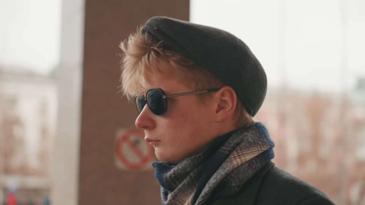Eftertænksom kaukasisk kreatør i profil, i et vinterligt bybillede, iført baret og solbriller, tørklæde og frakke i lag, blødt filmisk lys, eftertænksomt blik skifter mellem fotograf, digter, instruktør