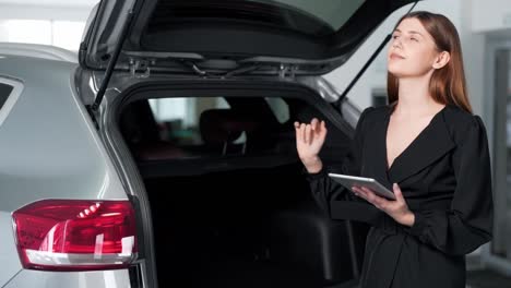 Hermosa-Mujer-Joven-Con-Una-Tableta-Mira-En-El-Maletero-De-Un-Coche