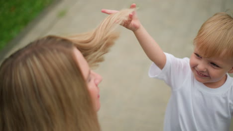 a joyful outdoor interaction between a mother and her son. the boy laughs while playfully touching his mother s hair as she touches his head