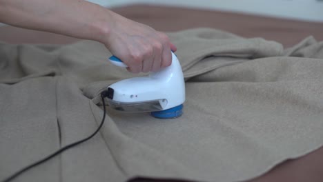 woman uses a machine for removing pellet and spools from clothes and fabric on black trousers. a modern electronic device for updating old things.