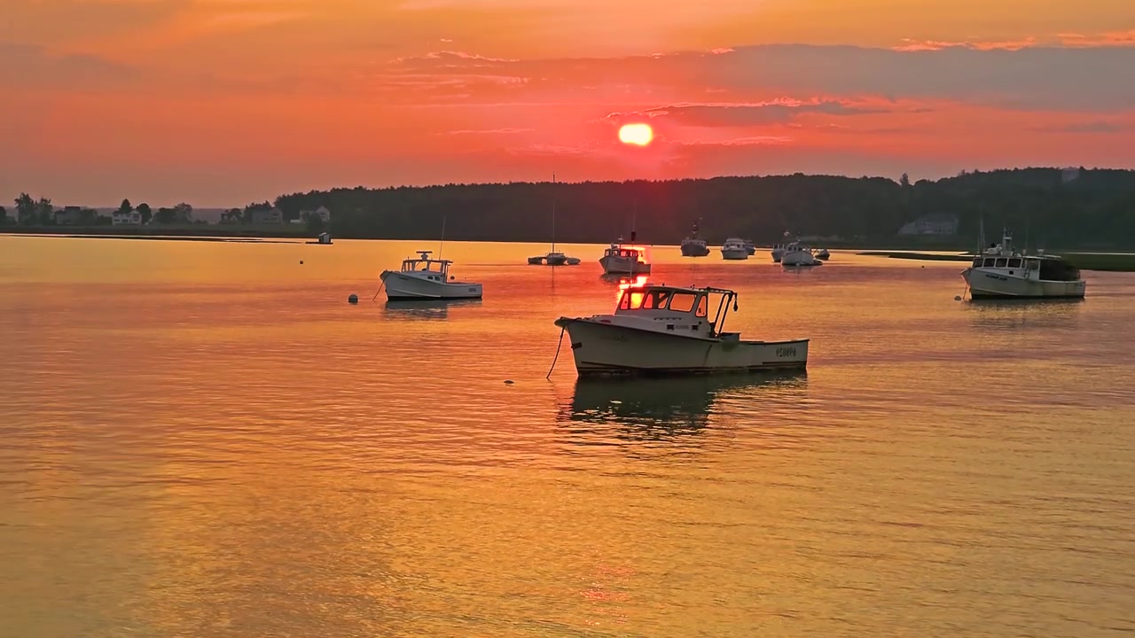 Belo porto costeiro ao pôr do sol com barcos de pesca, caminho de sol brilhante na água, céu de verão quente e atmosfera litorânea tranquila para vídeos de viagem ou natureza.