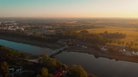 Una-Toma-Aérea-De-Un-Río-En-Polonia-Al-Amanecer-Con-Un-Puente-Verde-Y-Amarillo-Verde-En-El-Fondo