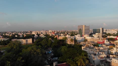 Volando-Sobre-La-Ciudad-De-Chennai-Temprano-En-La-Mañana-Viendo-Un-Pájaro-Volar-Frente-A-La-Cámara,-Casas-Y-árboles-Bañándose-En-La-Luz-Del-Sol-Temprano-En-La-Mañana