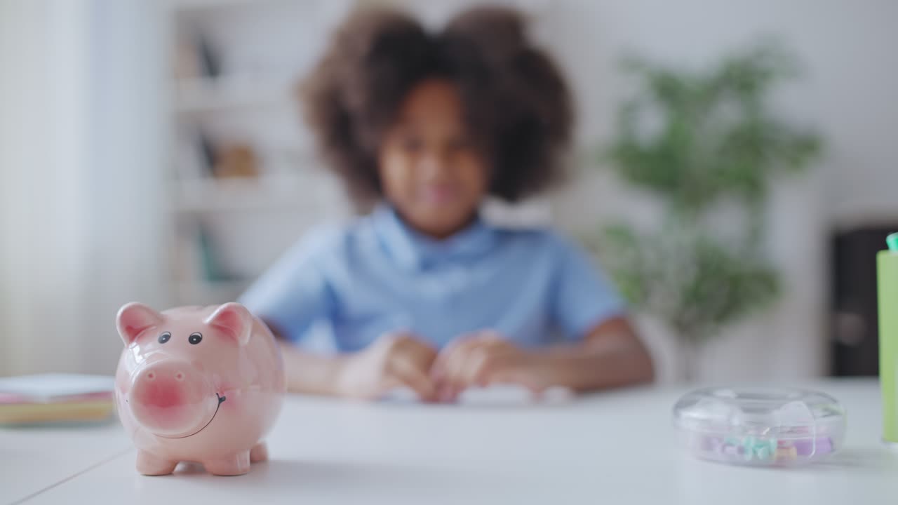 Smiling little girl putting coins into piggybank, learning to save money