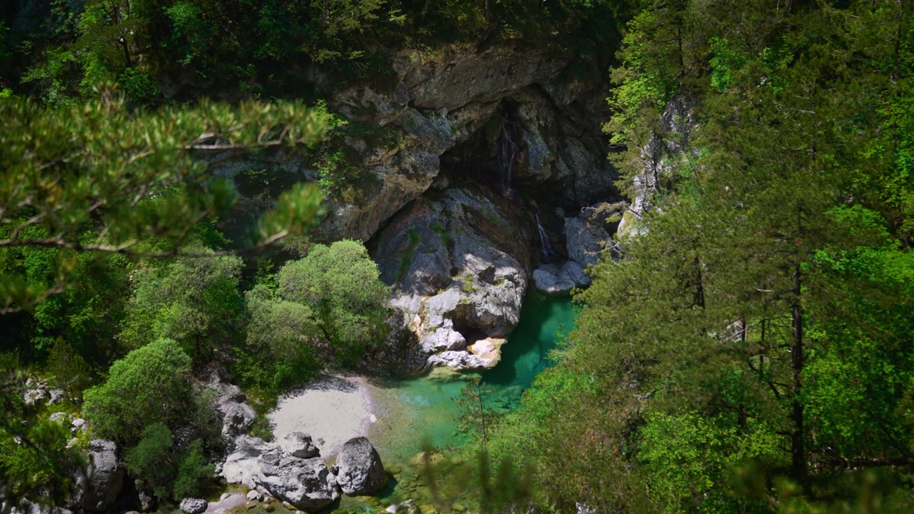 Cascata naturale che si getta in una pozza d'acqua verde trasparente circondata da scogliere alpine alle Pozze Smeraldine
