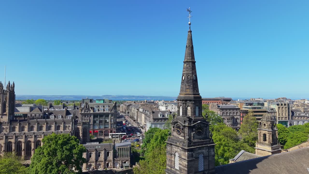 Drone orbit around St Cuthbert’s Tower at Edinburgh’s center, revealing the cityscape on a clear blue morning with vibrant details and bright skies
