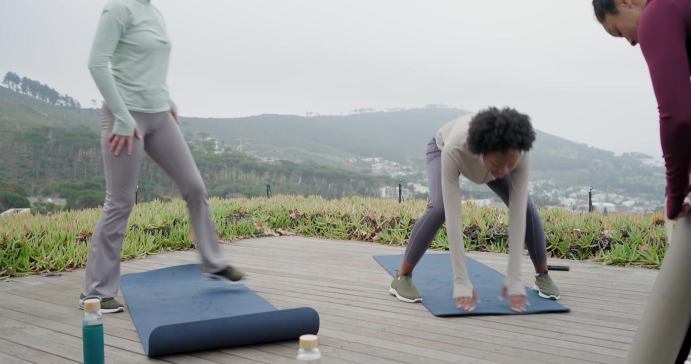 Amiche diverse che srotolano tappetini e posizionano bottiglie d'acqua su una terrazza sul tetto, preparandosi per l'allenamento.