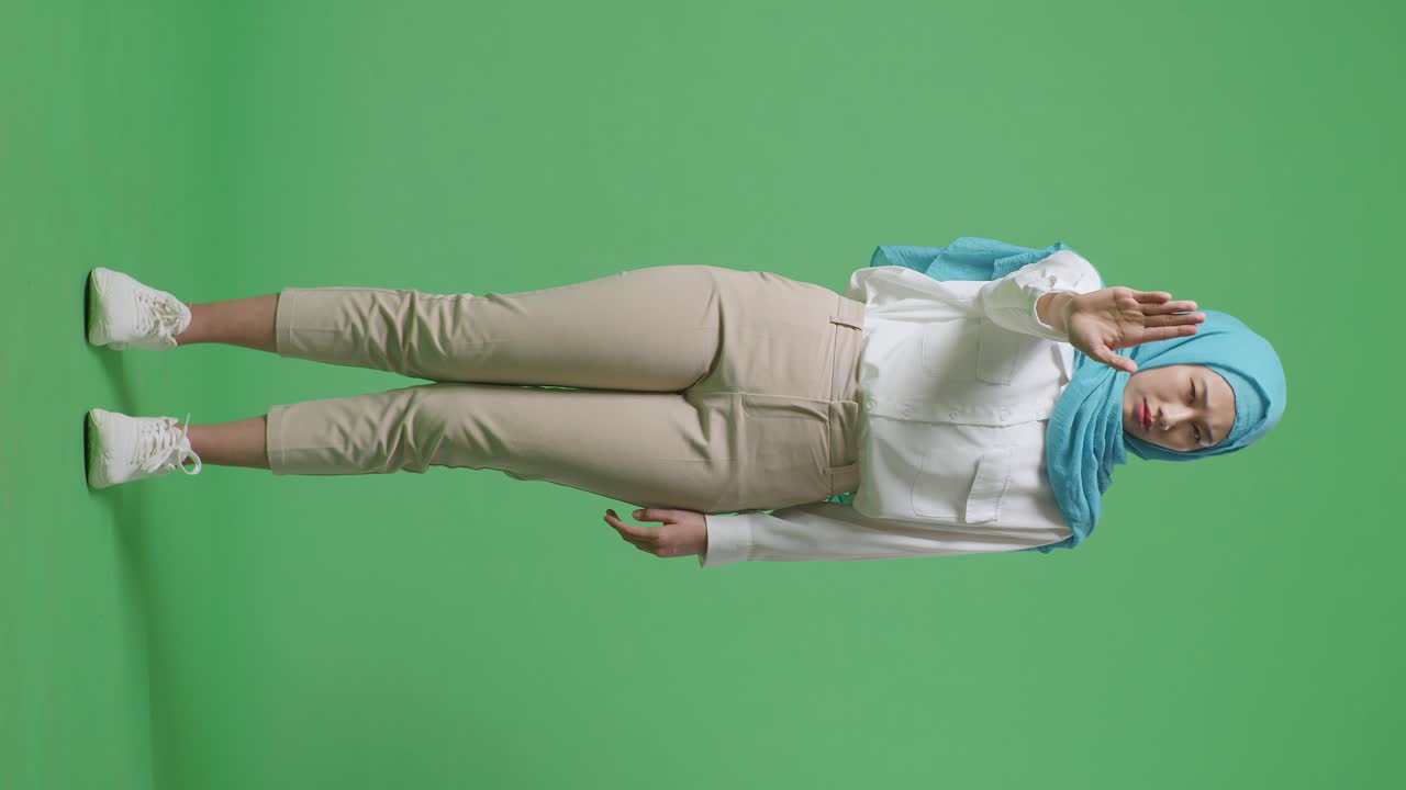 녹색 스크린 배경 스튜디오에 서있는 동안 손 표지 없이 불쾌감을 표하는 아시아 무슬림 여성의 몸