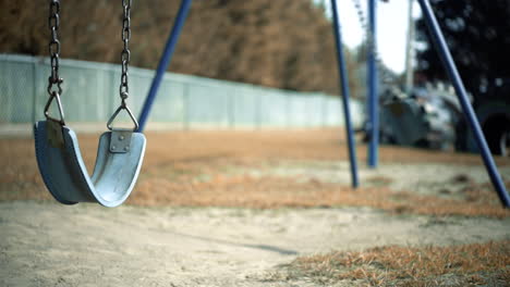 Abandoned-Empty-Swing-Set-Swings-Swaying-In-Wind-at-Children's-Playground-with-Fenceline-in-background-during-Autumn-Second-Swing-is-Moving-Faster-4K-ProRes