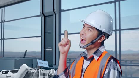 vista lateral de cerca de un ingeniero asiático con casco de seguridad de pie en una fábrica de alta tecnología, analizando el concepto de la máquina robótica. pensando en algo y mirando a su alrededor y luego levantando el dedo índice
