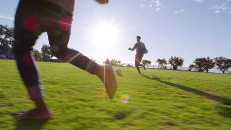 cuatro adultos jóvenes jugando al fútbol en un parque al atardecer