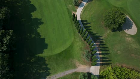 aerial birds eye view flying overhead green golf course fairway with path running in the middle