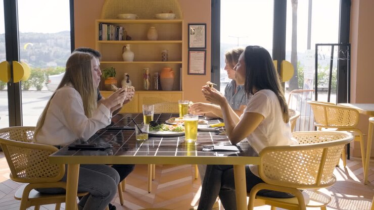 вид сбоку на группу друзей, разговаривающих и поедающих пиццу за столиком в ресторане