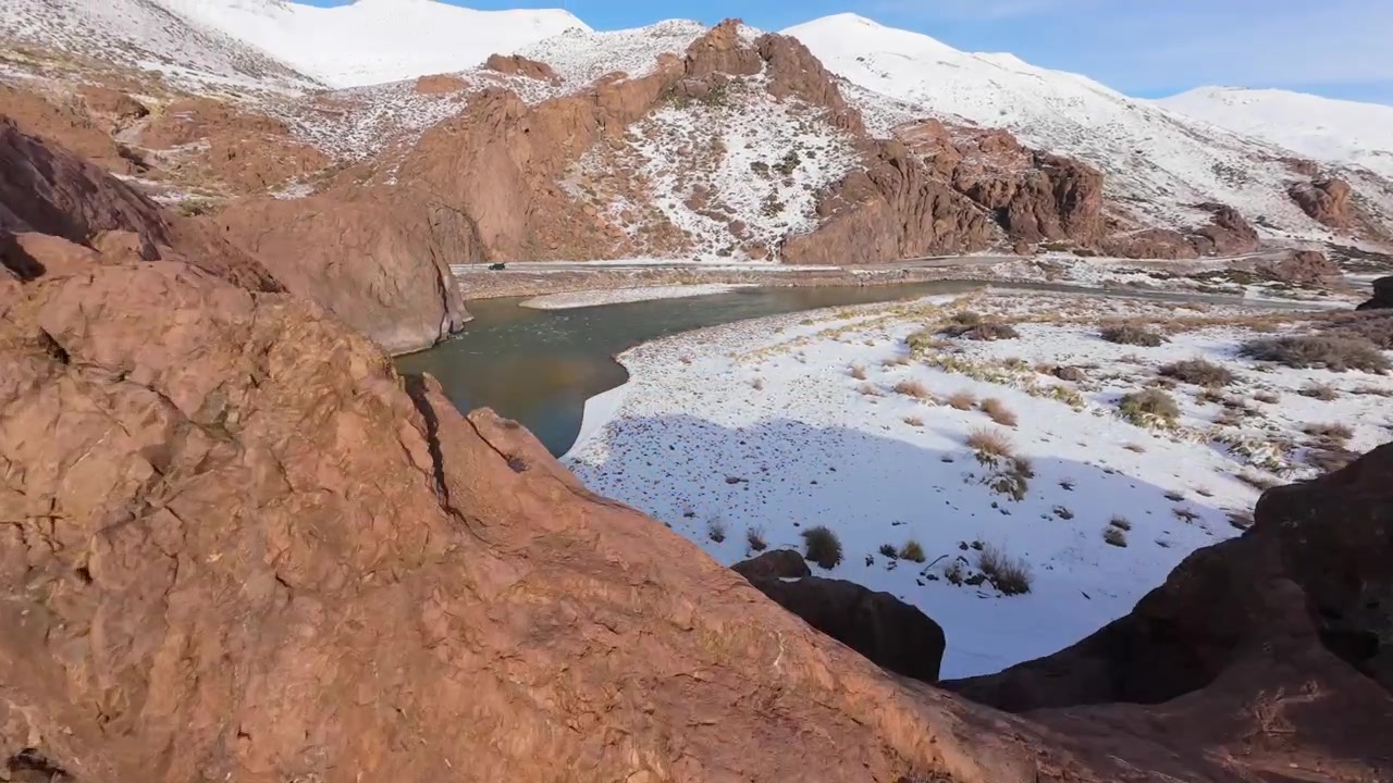Paso Pehuenche along RN145 in Mendoza, Argentina, showing volcanic rock formations, snowy mountain terrain and winding river valleys in the high Andes, FPV forward flight and orbit shot.