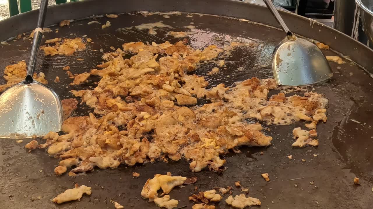 A close-up view of bean sprouts being mixed into a sizzling omelet on a large pan.