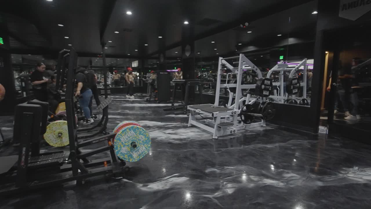 People working out in a modern, dark-themed gym with various exercise equipment