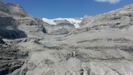 una foto aérea de pequeñas cascadas y un glaciar lejano en la cima de una montaña en verano