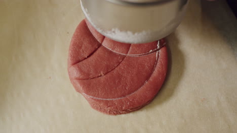 a person hand pressing down on a red cookie dough making designs, close up static