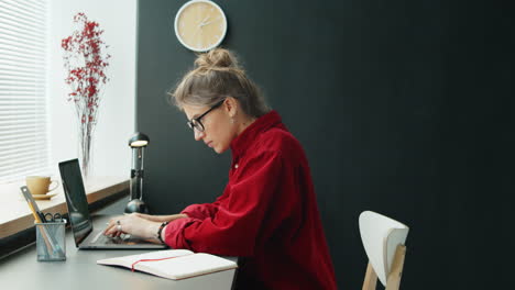 Businesswoman-Using-Laptop-and-Taking-Notes-in-Office