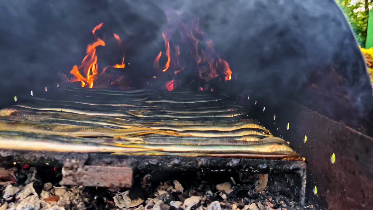 Eel fish roasting over charcoal fire inside outdoor smoker grill