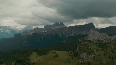 Aerial-view-with-distant-steep-tall-mountains-in-the-background-green-forest-with-valley-between-mountains,-before-storm,-rainy-day,-cinematic-grade