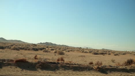 driving quickly down a dirt road in the middle of the desert with mountains in the distance and dry shrubs passing by