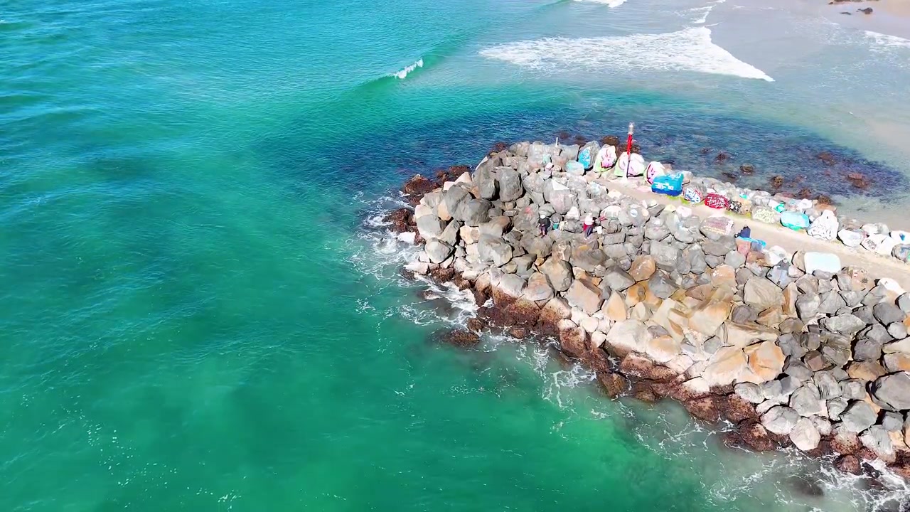 Port Macquarie'de taş bir dalgakırana çarpan turkuaz dalgaların yüksek açılı drone çekimi.
