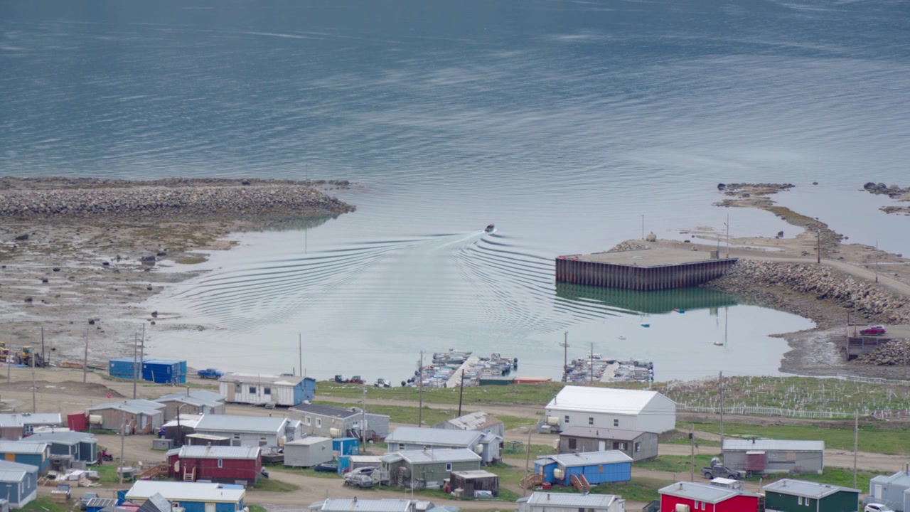 Pangnirtung küçük tekne limanının korunaklı havzasında, engebeli kıyı şeridi boyunca demirlemiş küçük motorlu teknelerin ve yerel İnuit balıkçı teknelerinin geniş görünümü