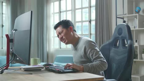 asian man in long sleeved t-shirt having backache while using desktop computer for working at home.