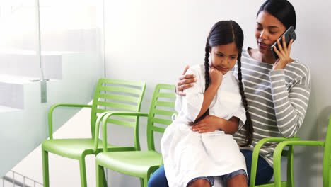 Mother-talking-on-mobile-phone-while-girl-sits-on-her-lap