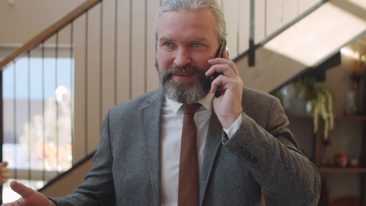 Starší podnikatel se prochází v kanceláři a telefonuje