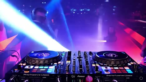 dj mixes music on a console in front of an energetic nightclub audience. colorful lights flash in the background, enhancing the vibrant atmosphere of the performance