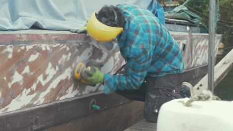 a man sanding a wooden boat hull using an orbital sander