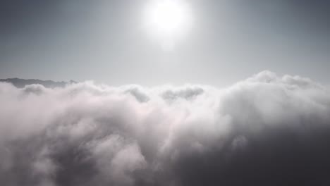 Vista-Aérea-Ascendente-Por-Encima-De-Una-Espesa-Capa-De-Nubes,-Con-El-Sol-Brillando-Por-Encima-De-Las-Nubes