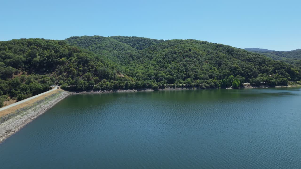 An afternoon aerial view of Uvas Reservoir shows golden hills rippling beside still, reflective water