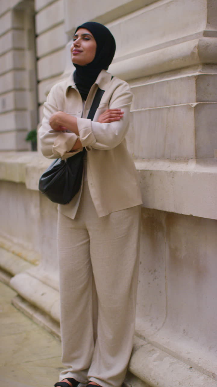 Vertical Video Portrait Of Smiling Muslim Businesswoman Wearing Hijab And Modern Business Suit Standing And Folding Arms Outside City Office Buildings 2